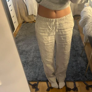 Beiga linnebyxor från Arket - Säljer ett par ljusa beiga linnebyxor från Arket med resår och snörning i midjan. Byxorna har raka ben och sidfickor, perfekta för en chill och avslappnad stil. Materialet är svalt och luftigt linne, vilket gör dem sköna under varmare dagar.