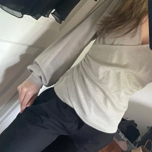 Glittrig omlottopp från Stockh LM  - Supersnygg glittrig topp i silver från Stockh LM. Omlottmodell med v-ringning och långa luftiga ärmar. Sitter figurnära och har en lyxig känsla med sitt skimrande material. Perfekt för dig som vill sticka ut lite extra. Tröjan är endast använd en gång!!