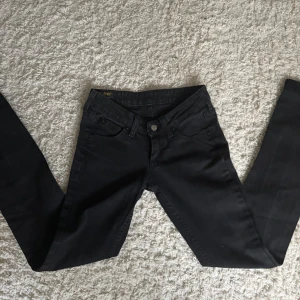 Svarta jeans från Lee - Svarta jeans från Lee med klassisk femficksdesign och straight  passform. Jeansen har normal midja och är tillverkade i ett stretchigt bomullsmaterial för en bekväm känsla. Snygga detaljer med Lee-logga på bakfickan och metallknapp framtill.