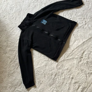 Svart bomberjacka från Overload - Svart bomberjacka från Overload med blått broderat tryck 'Overload 29' på bröstet. Jackan har ribbade muddar vid krage, ärmslut och nederkant samt dragkedja framtill. Två snedställda fickor och sportig collegekänsla. Perfekt för dig som gillar streetwear.