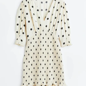 Prickig kortklänning från H&M - Supersöt kortklänning i ljusbeige med svarta prickar från H&M. Djup v-ringning, trekvartsärmar med resår och volangdetalj nertill. Smockad midja ger en snygg passform. Perfekt för dig som gillar lekfulla och trendiga plagg.
