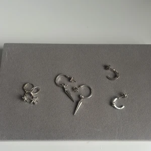 3 par silvriga örhängen  - Säljer tre par silvriga örhängen: ett par med små stjärnhängen och glittrande sten, ett par med  spikes och ett par ringar med liten sten. Ursprungligen köpta som 4-par från Kappahl men använder endast 1 av dem. De som säljs är aldrig använda!!