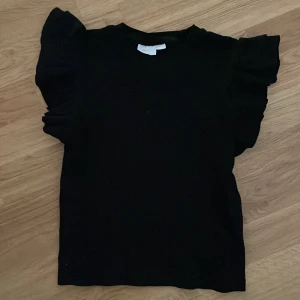 Svart topp med volangärmar Gina Tricot - Supersnygg svart topp från Gina Tricot med volangdetaljer på ärmarna. Perfekt att styla med jeans eller kjol för en enkel men stilren outfit.💗💗 skriv vid fundering 