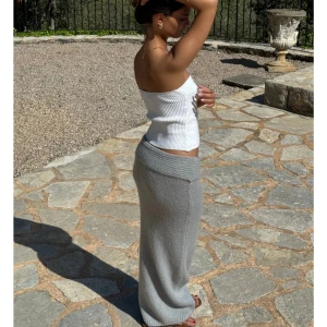 Grå stickad maxikjol från Design by Si - Supermjuk och lång grå stickad kjol från Sefina med bred, vikt midja. Kjolen har en loose passform och är perfekt trendig look. Kjolen är helt i nyskick och har inte används då den var för kort. OBS rekommenderas för en person som ungefär är 160 cm lång om man vill ha den så lång som på bilden