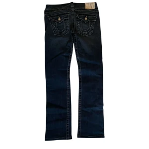 True Religion Billy jeans - Snygga mörkblå jeans från True Religion. Jeansen är low waist med lite av en bootcut passform. Skicka meddelande vid frågor. Väldigt bra skick, plagget har inga defekter eller fläckar✔️                                    📏Mått: Midja tvärs över 36,5 cm, innerbens längd 74 cm, benöppning 19 cm. 📏