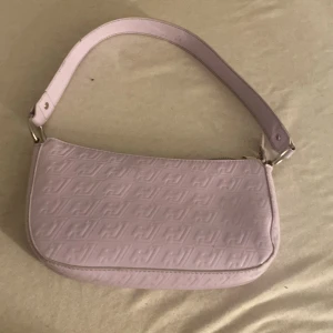 Ljuslila axelväska med präglat mönster - Säljer en ljuslila axelväska med präglat mönster över hela väskan. Väskan har en kort axelrem och stängs med dragkedja. Perfekt för dig som gillar stilrena accessoarer med en twist av färg.
