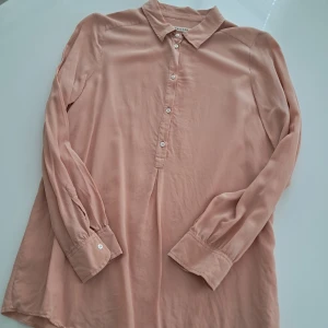 Ljusrosa silkesskjorta från Masscob i Siden.  - Superfin ljusrosa skjorta från Masscob i 100% silke. Skjortan har klassisk krage, knappar framtill och långa ärmar med manschett. Snygg, flowy passform som känns lyxig och skön mot huden. Perfekt för dig som gillar stilrena och mjuka plagg.