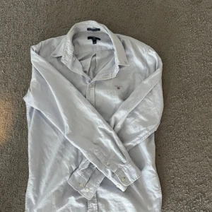 Ljusblå Oxfordskjorta från Gant - Snygg ljusblå Oxfordskjorta från Gant med klassisk krage och knäppning framtill. Skjortan har broderad Gant-logga på bröstet och är tillverkad i bomull. Perfekt för dig som gillar stilrena och tidlösa plagg.