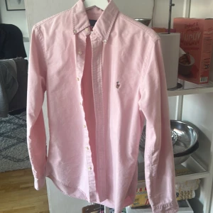 Rosa skjorta från Ralph Lauren slim fit - Säljer en stilren rosa skjorta från Ralph Lauren i slim fit-modell. Skjortan har klassisk button down-krage, broderad logga på bröstet och är tillverkad i mjuk bomull. Perfekt för dig som gillar en clean och fräsch look. Jag säljer för den inte längre passar. Nästan oanvänd.
