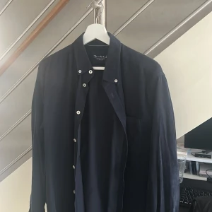 Mörkblå manchesterskjorta Bondelid - Snygg mörkblå skjorta från Bondelid i manchester med klassisk krage och vita knappar. Skjortan har lång ärm och en bröstficka, perfekt för en stilren look. Skräddad passform som sitter riktigt bra.
