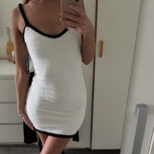 Vit stickad miniklänning från NA-KD - Superfin vit stickad miniklänning från NA-KD med svarta kontrastkanter. Klänningen har smala axelband och en figurnära passform. Med prislapp.  