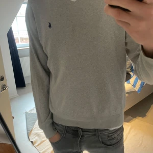 V-neck från Polo Ralph Lauren - Snygg grå tröja från Polo Ralph Lauren i mjuk pima bomull. Klassisk v-ringning och diskret broderad logga på bröstet. Funkar både vardagligt och till finare tillfällen, hör av er vid frågor