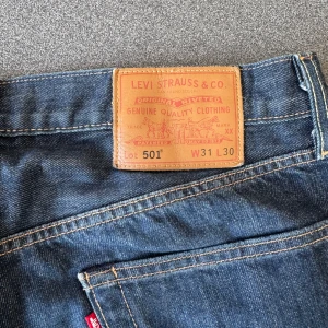 Levi's 501 jeans blå W31 L30 - Klassiska Levi's 501 jeans i mörkblå denim med raka ben och normal passform. Byxorna har fem fickor, knappgylf och tydliga kontrastsömmar. Perfekta för en avslappnad och tidlös look.