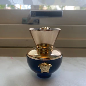 Versace Dylan Blue Pour Femme parfym - Exklusiv parfymflaska från Versace, Dylan Blue Pour Femme. Flaskan är rund och djupblå med lyxiga gulddetaljer och Medusa-emblem både framtill och på locket. Den har en unik, elegant form och känns riktigt lyxig på sminkbordet. 30 ml, använd ca 2-3 gånger. 