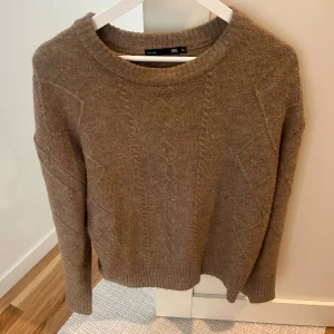 Beige stickad tröja  - Mysig beige stickad tröja från Lager 157!  Tröjan har ett kabelstickat mönster framtill och ribbade muddar vid ärmslut och nederkant. 