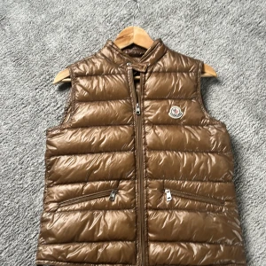 Brun dunväst från Moncler - Säljer en moncler väst. Modellen är från 2011 så de är därför jag säljer den billigare och så kan de se lite konstig ut men den är såklart äkta!