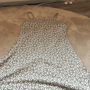 Blommig sommarklänning med smala axelband från New - Supersöt blommig klänning med smala axelband från New. Klänningen är vit med små svarta blommor och har en lätt utställd passform. Har nån liten fläck men inte så att man lägger märke till de, hör av dig vid intresse eller frågor❤️