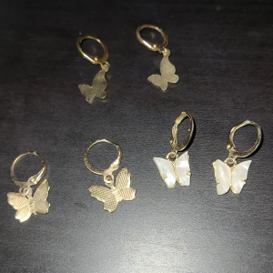 Guldiga örhängen med fjärilar,  3st - Tre par örhängen i guldton med fjärilsberlocker. Ett par har släta fjärilar, ett par har mönstrade fjärilar och ett par har vita fjärilar med guldiga detaljer. Perfekta för att mixa och matcha till olika outfits.