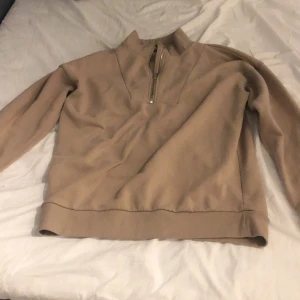 Beige halvzip tröja från Denim Day - Säljer en beige långärmad tröja från Denim Day i storlek S. Tröjan har halv dragkedja vid halsen och är tillverkad i mjukt material. Perfekt för lager-på-lager och enkel att matcha med olika outfits.