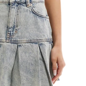 Volang jeanskjol  - Säljer en ljusblå jeanskjol med plisserad design och rå kant nertill. Kjolen har klassiska jeansdetaljer som bälteshällor och fickor. Perfekt för dig som gillar en trendig och avslappnad stil.