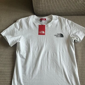 Vit t-shirt från The North Face - Säljer en klassisk vit t-shirt från The North Face med logga tryckt på bröstet. T-shirten har rund halsringning och korta ärmar. Perfekt basplagg med enkel och stilren design.
