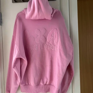 Rosa hoodie från LXA The Label - Säljer en oversized rosa hoodie från LXA The Label med broderad logga på ryggen. Tröjan har huva med dragsko och breda muddar vid ärmslut och nederkant. Perfekt för en avslappnad stil. Storlek M. Använd 2 gånger, fortfarande som ny.