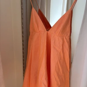 Orange randig klänning med smala axelband - Säljer en orange klänning med vita smala ränder och tunna axelband. Klänningen har v-ringad halsringning och är ärmlös, perfekt för varma dagar. Lätt och luftig modell som ger en somrig känsla. Säljer pga inte riktigt min färg, har samma i storlek S om någon skulle vara intresserad!💞
