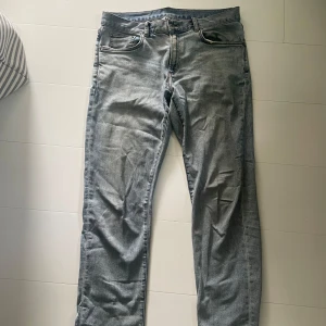 Ljusblå jeansbyxor - Säljer ett par klassiska ljusblå jeans med fem fickor och raka ben. Byxorna har normal passform och stängs med dragkedja och knapp. Perfekta till vardags och enkla att matcha med olika stilar.