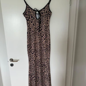 Leopardmönstrad långklänning med knyt - Säljer en snygg långklänning med leopardmönster i beige och svart. Klänningen har smala axelband, knytning framtill och en figurnära passform. Perfekt för dig som vill sticka ut med ett djurmönster!