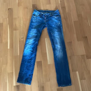 Dsquared Jeans W29 L32 - Säljer ett par blå jeans med coola slitningar och färgstänk. De har en klassisk femficksdesign och knappgylf. Perfekta för en avslappnad stil.
