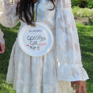 Studentklänning - Vit blommig omlottklänning med volang - Har enbart använts en gång och är i mycket bra skick!Superfin vit kortklänning med blommigt mönster och volangdetaljer. Klänningen har långa, vida ärmar och omlott-skärning framtill. Perfekt för sommarens alla tillfällen!