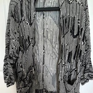 Svartvit mönstrad overshirt - Säljer en oversized svartvit overshirt med grafiskt randigt och abstrakt mönster. Jackan har lång ärm och öppen front utan synliga knappar eller dragkedja. Perfekt för att addera en cool touch till din outfit.