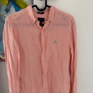 Ljusrosa linneskjorta från Gant - Säljer en ljusrosa skjorta från Gant i linne med broderad logga på bröstet. Skjortan har klassisk krage, knappar framtill och långa ärmar. Perfekt för en fräsch och stilren look!
