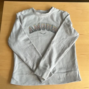 Ljusblå & svagt grå långärmad tröja från Zadig & Voltaire - Säljer en ljusgrå långärmad tröja från Zadig & Voltaire med texten 'AMOUR' i glittriga stenar framtill. Använd 2 ggr pga för liten! Nypris ca 1250 kr