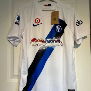 Inter Milan bortatröja 2023/24 Teenage Mutant Ninja Turtles -  Inter Milan bortatröja med blå och svart diagonal rand, klubbmärke och Serie A-logga. Unikt tryck med Teenage Mutant Ninja Turtles på bröstet. 