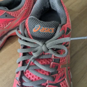 Rosa löparskor från Asics - Säljer ett par rosa och gråa löparskor från Asics med mesh-överdel och snörning. Skorna har en sportig design med dämpad sula och grå detaljer. Perfekta för träning eller löpning.