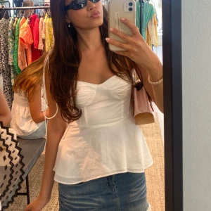 Vit topp med volang från Zara - Säljer en söt vit topp från Zara med volang nertill och smickrande passform. Toppen har breda axelband och lätt rynk vid bysten. Perfekt till sommaren och passar till både kjol och jeans.