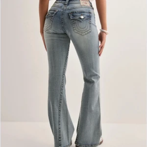 Ljusblå bootcut jeans från True Religion - Säljer ett par ljusblå jeans från True Religion med bootcut-passform och snygga detaljer på bakfickorna. Jeansen har låg midja, klassisk femficksdesign och kontrastsömmar. Perfekta för dig som gillar en avslappnad men trendig look. Köptes för 1399kr 