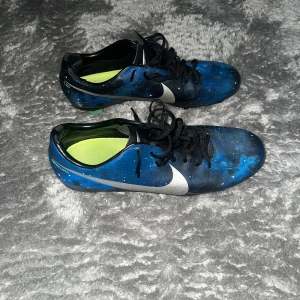 Nike mercurial CR7 galaxy - Säljer ett par blå Nike fotbollsskor med unikt galaxmönster och stora silvriga swoosh-loggor på sidorna. Skorna har svarta snören och gröna dobbar undertill. Perfekta för dig som vill sticka ut på planen!