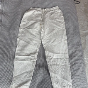 Vita linnebyxor från Holly & Whyte - Säljer ett par vita linnebyxor från Holly & Whyte med resår och snörning i midjan. Byxorna har raka ben och är perfekta för varma dagar. Lätta och luftiga med fickor fram och bak.