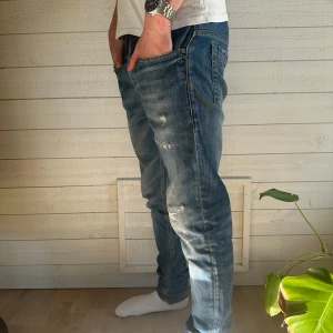 Dondup George jeans - Säljer ett par blå jeans med coola slitningar och en klassisk femficksdesign. De har en normal passform och är perfekta för en avslappnad stil. Jeansen är använda fåtal gånger, och i bra skick. Original pris 2000kr mitt pris 799