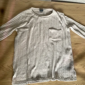 Beige ribbad långärmad tröja från Gina Tricot - Säljer en beige ribbad trekvartsärmad tröja från Gina Tricot. Tröjan har rund halsringning, en liten bröstficka och är i ett mjukt, stretchigt material. Perfekt för lager-på-lager och enkel att matcha med olika outfits.