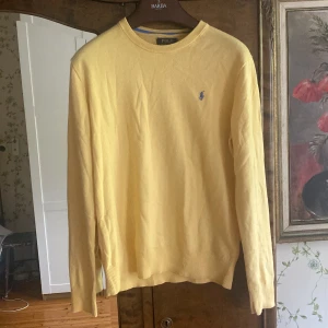 Polo Ralph Lauren tröja - Snygg gul långärmad tröja från Polo Ralph Lauren med klassisk blå logga broderad på bröstet. Tröjan är i mjuk bomull och har ribbade muddar vid ärmslut och nederkant. Perfekt för en stilren och avslappnad look. Passar S/M