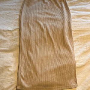 Beige ribbad långkjol - Säljer en beige ribbad långkjol med rak passform. Kjolen är stretchig och har en mjuk känsla, perfekt för en avslappnad men ändå stilren look. Passar till många olika outfits och är superenkel att matcha.