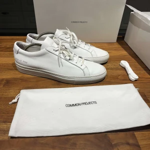 Vita sneakers från Common Projects - Ett par skor från Common projects, Achilles Low White, som använts mindre än 10 gånger. Jag säljer på grund av de inte passar mig. Storlek 42 (lite stor i storlek), passar säkert 43. Bevis på att de är äkta finns och medföljer, om man vill ha mer bevis på att de är äkta skriv personligen. Skolåda, påse och skosnöre ingår.