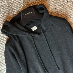 Rose & Born Kashmir hoodie - Säljer en svart hoodie i mjuk kashmir från Rose & Born. Tröjan har huva med dragsko och långa ärmar. Perfekt för dig som gillar stilrena och bekväma plagg med exklusiv känsla. Notera även defekten på vänstra ärm som är ihopsydd fint syns inte vid användning 