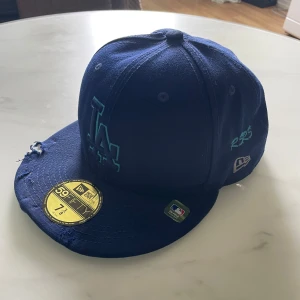 Blå LA Dodgers keps från New Era - Säljer en blå LA Dodgers keps från New Era 59FIFTY-kollektionen. Kepsen har broderad LA-logga framtill och MLB-märke på sidan. Klassisk rak skärm och justerbar passform. Perfekt för dig som gillar sportig stil.