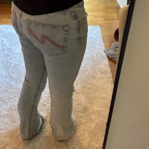 Ljusblå bootcut jeans med broderade bakfickor - Säljer ett par ljusblå bootcut jeans med slitna hål på knäna och broderade detaljer på bakfickorna. De är från Nelly i storlek 34❤️ de har ett litet hål vid insida lår men inget som märks när man har på sig dem