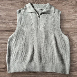 Ljusgrå stickad väst med dragkedja från Stories - Ljusgrå stickad väst från Stories i storlek XL. Västen har en kort dragkedja framtill och en hög krage. Perfekt att bära över en skjorta eller tröja för en trendig lager-på-lager-look.