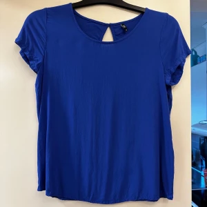 Blå blus från ONLY - Säljer en blå blus från ONLY med rund halsringning och korta ärmar. Toppen har en liten öppning med knapp i nacken som detalj. Perfekt till sommargarderoben och enkel att matcha med olika underdelar. Storlek 36. Aldrig använd. 